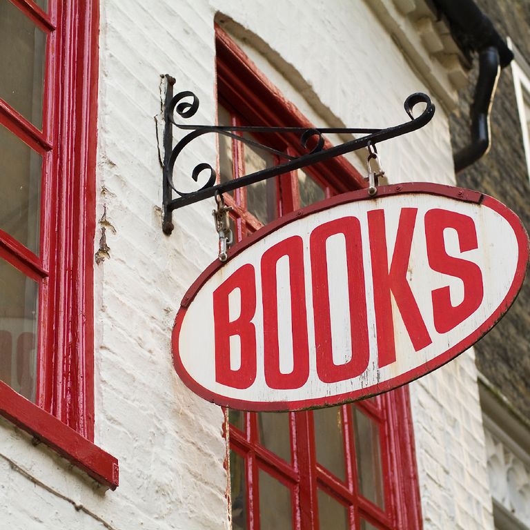 Books-Schild hängt an einer weißen Hausfassade zwischen zwei roten Fenstern.