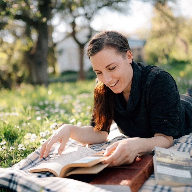 Susann liegt auf ihrer Lieblingswiese im Garten und liest lächelnd ein Buch.