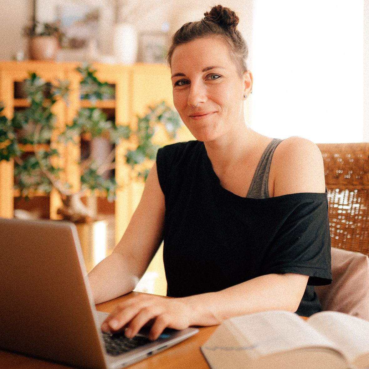 Susann Pacher sitzt am Laptop und lächelt in die Kamera. 