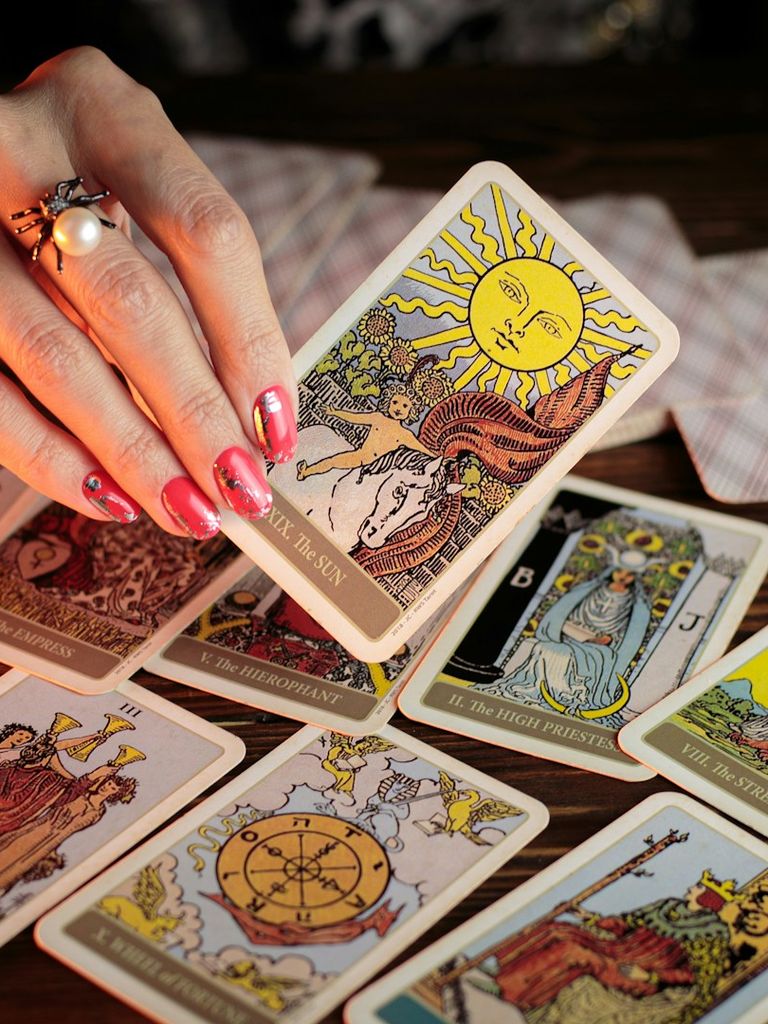Waite-Tarotkarten liegen auf einem Tisch. Eine esoterisch wirkende Hand links im Bild hält die Sonne in die Kamera.