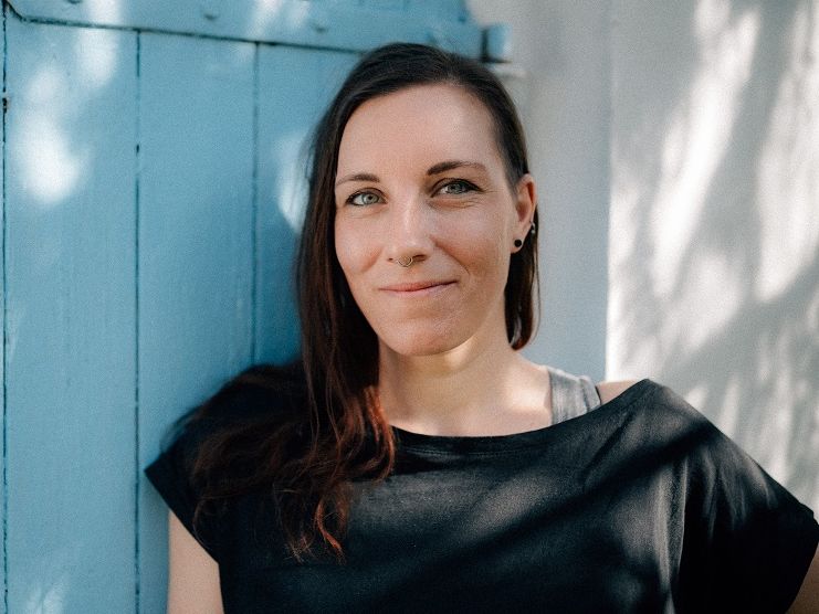 Susann Pacher vor blauer Holztür in die Kamera lächelnd