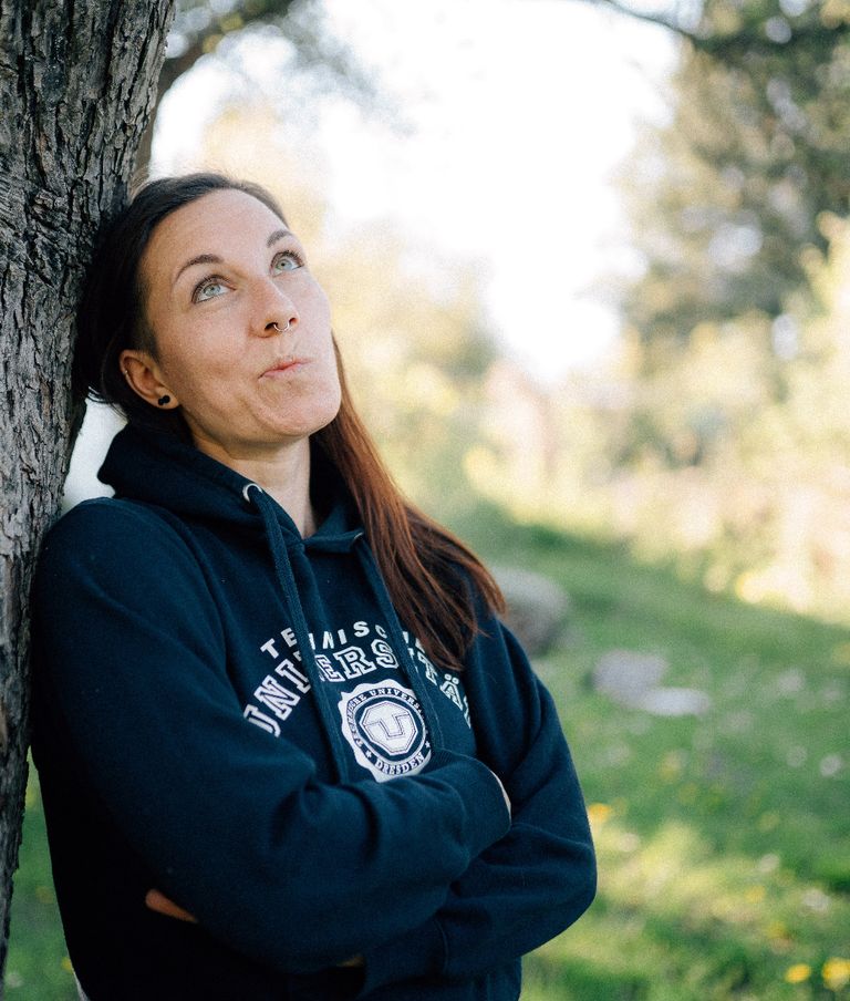 Susann lehnt an einem Baum und verzerrt nachdenklich ihr Gesicht. Wirkt nicht sehr vorteilhaft. Sie trägt einen TU-Dresden-Pulli